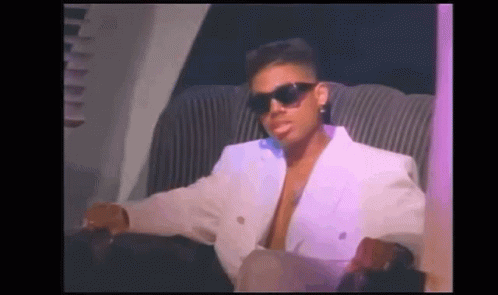 A Man Wearing Sunglasses And A White Jacket Is Sitting In A Chair . GIF