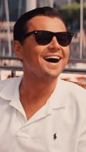 A Man Wearing Sunglasses And A White Polo Shirt Is Laughing . GIF