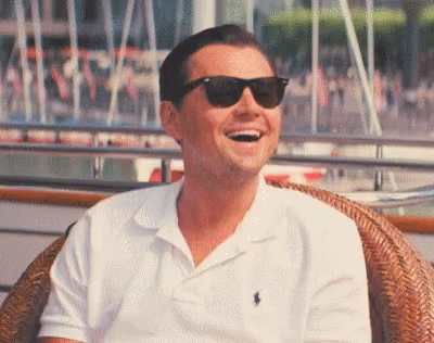 A Man Wearing Sunglasses And A White Polo Shirt Is Sitting In A Chair And Laughing . GIF