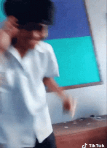 A Man Wearing Sunglasses And A White Shirt Is Dancing In Front Of A White Board That Says Tik Tok On It GIF