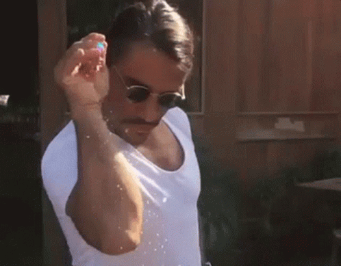 A Man Wearing Sunglasses And A White Shirt Is Holding A Balloon In His Hand . GIF