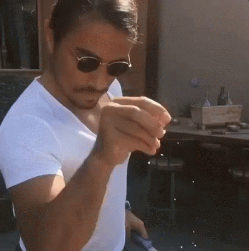 A Man Wearing Sunglasses And A White Shirt Is Holding A Piece Of Food In His Hand . GIF