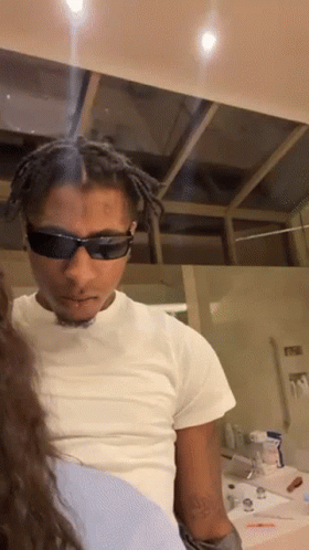 A Man Wearing Sunglasses And A White Shirt Is Looking At A Woman GIF
