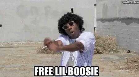 A Man Wearing Sunglasses And A White Shirt Is Standing In A Dirt Field And Says `` Free Lil Boosi '' . GIF