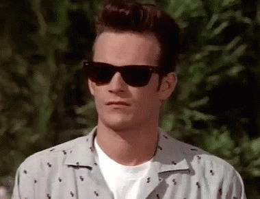 A Man Wearing Sunglasses And A White Shirt Is Standing In Front Of A Tree . GIF