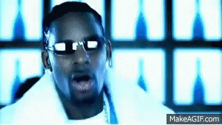 A Man Wearing Sunglasses And A White Shirt Is Standing In Front Of A Wall With A Blue Light Behind Him . GIF