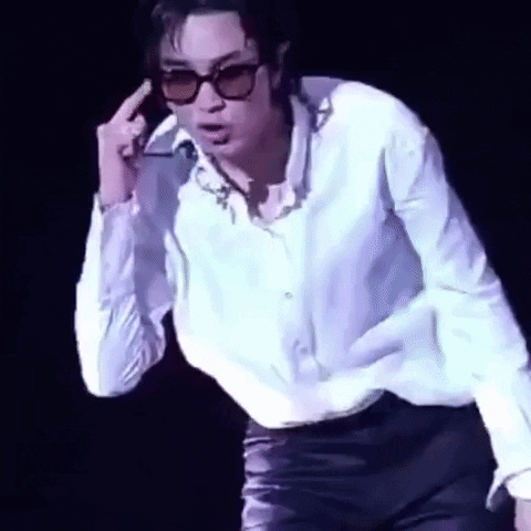 A Man Wearing Sunglasses And A White Shirt Is Standing On A Stage And Giving The Middle Finger . GIF