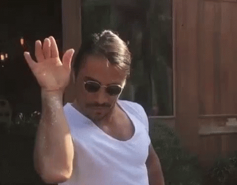 A Man Wearing Sunglasses And A White Shirt Is Waving His Hand In Front Of A Window . GIF