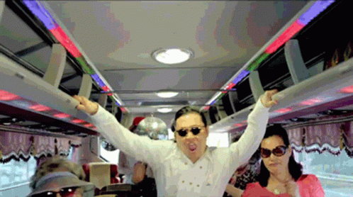 A Man Wearing Sunglasses And A White Shirt Stands In A Bus With His Arms Outstretched GIF