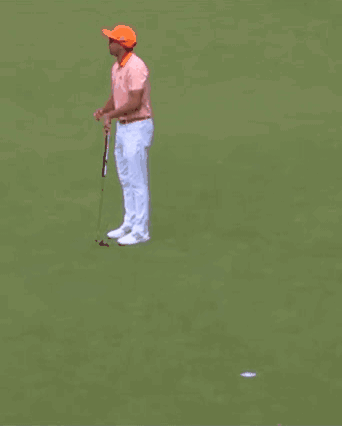 A Man Wearing Sunglasses And An Orange Hat Is Standing In Front Of A Crowd Holding A Golf Club . GIF