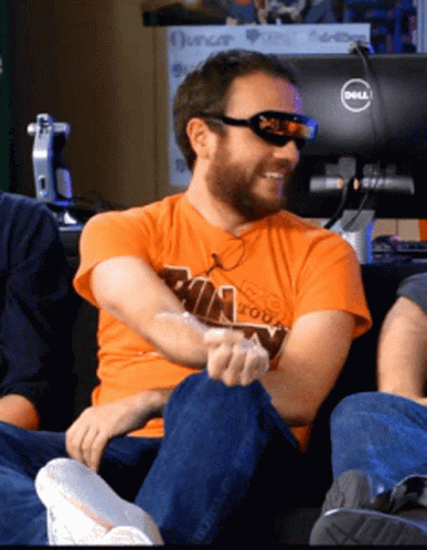 A Man Wearing Sunglasses And An Orange Shirt Sitting In Front Of A Dell Monitor GIF