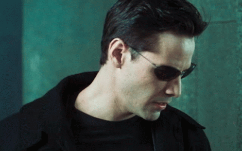 A Man Wearing Sunglasses And Ear Buds Looks Down GIF