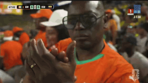 A Man Wearing Sunglasses Applauds During A Soccer Match GIF