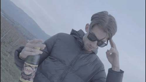 A Man Wearing Sunglasses Holds A Bottle Of Diago GIF