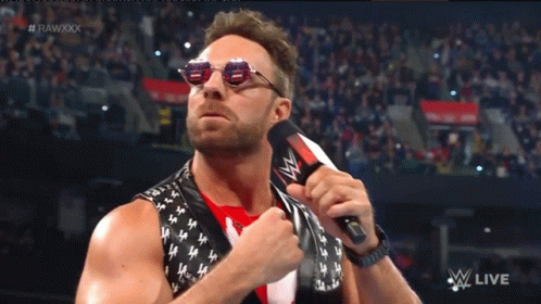 A Man Wearing Sunglasses Holds A Microphone In Front Of A Crowd And The Words Rawxxx Are Visible GIF