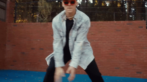 A Man Wearing Sunglasses Is Dancing In Front Of A Red Brick Wall GIF