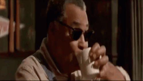 A Man Wearing Sunglasses Is Drinking A Cup Of Coffee In A Restaurant . GIF
