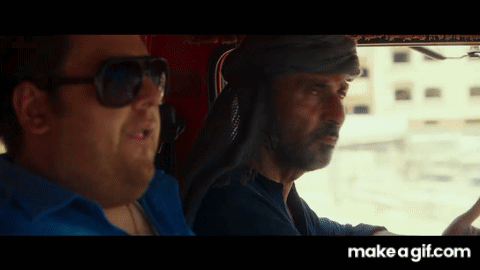 A Man Wearing Sunglasses Is Driving A Car Next To Another Man GIF
