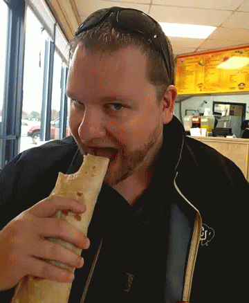 A Man Wearing Sunglasses Is Eating A Burrito With The Letter J On His Jacket GIF