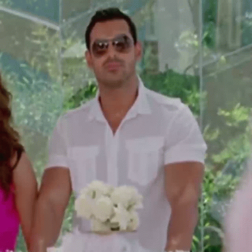 A Man Wearing Sunglasses Is Holding A Bouquet Of Flowers . GIF