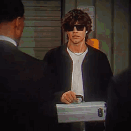A Man Wearing Sunglasses Is Holding A Briefcase While Talking To A Man In A Suit . GIF