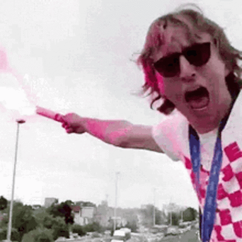 A Man Wearing Sunglasses Is Holding A Flare In His Hand And Pointing . GIF