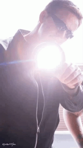 A Man Wearing Sunglasses Is Holding A Flashlight In His Hand GIF