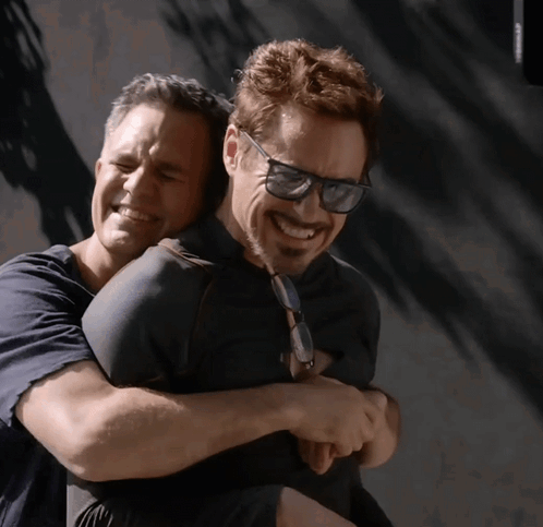 A Man Wearing Sunglasses Is Hugging Another Man Who Is Smiling GIF