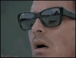 A Man Wearing Sunglasses Is Looking Down At Something . GIF