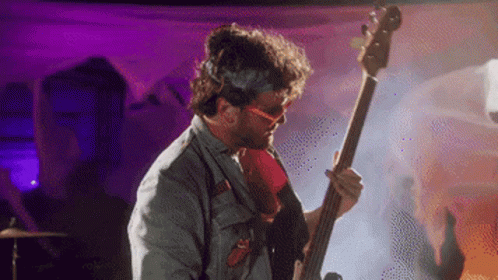 A Man Wearing Sunglasses Is Playing A Bass Guitar GIF