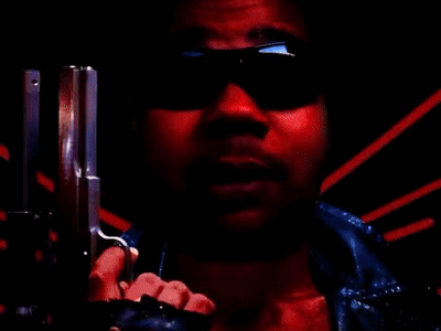 A Man Wearing Sunglasses Is Pointing A Gun At The Camera In A Red Background . GIF