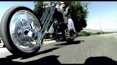 A Man Wearing Sunglasses Is Riding A Motorcycle On A Street GIF