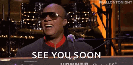 A Man Wearing Sunglasses Is Singing Into A Microphone And Saying `` See You Soon '' While Playing A Keyboard . GIF