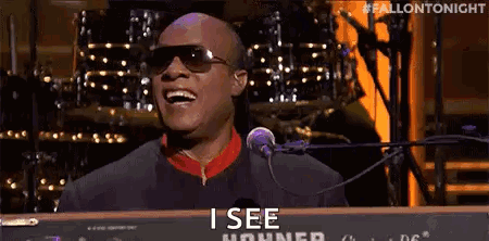 A Man Wearing Sunglasses Is Singing Into A Microphone While Playing A Piano . GIF