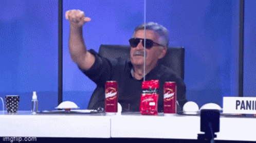 A Man Wearing Sunglasses Is Sitting At A Table With Two Red Cans Of Budweiser GIF