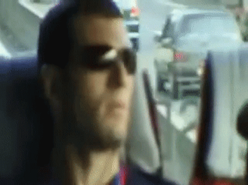A Man Wearing Sunglasses Is Sitting In A Car Looking Out The Window GIF