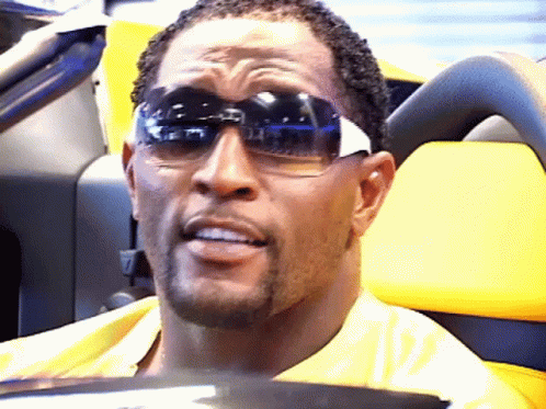 A Man Wearing Sunglasses Is Sitting In A Yellow Vehicle GIF