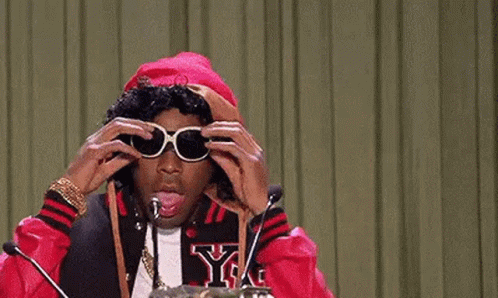 A Man Wearing Sunglasses Is Sitting In Front Of A Microphone And Talking Into It . GIF