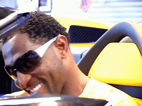 A Man Wearing Sunglasses Is Smiling In A Yellow Car GIF