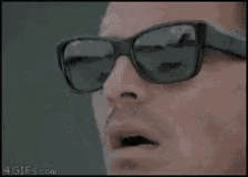 A Man Wearing Sunglasses Is Smoking A Cigarette And Looking At The Camera . GIF