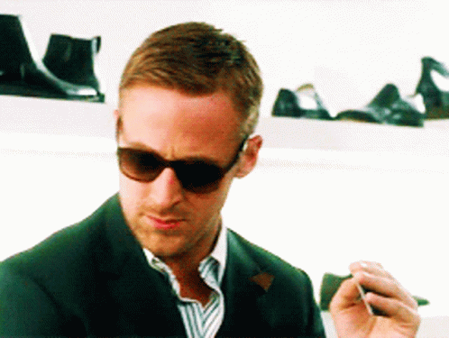 A Man Wearing Sunglasses Is Smoking A Cigarette In Front Of A Shoe Display GIF