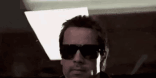 A Man Wearing Sunglasses Is Standing In A Dark Room . GIF
