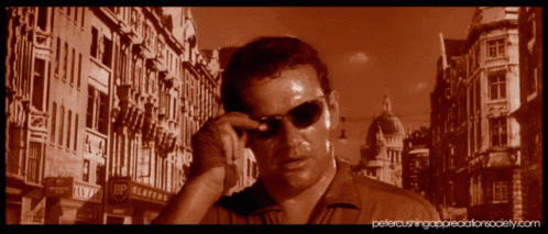 A Man Wearing Sunglasses Is Standing In Front Of A Building That Says Bp Platters GIF