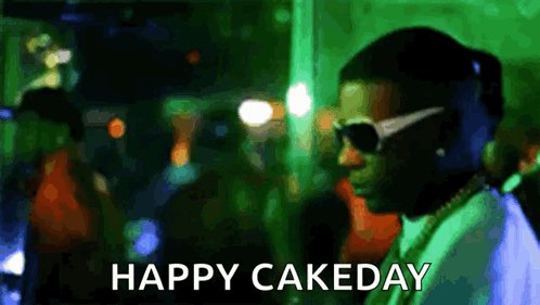 A Man Wearing Sunglasses Is Standing In Front Of A Crowd With The Words Happy Cakeday Written Below Him . GIF