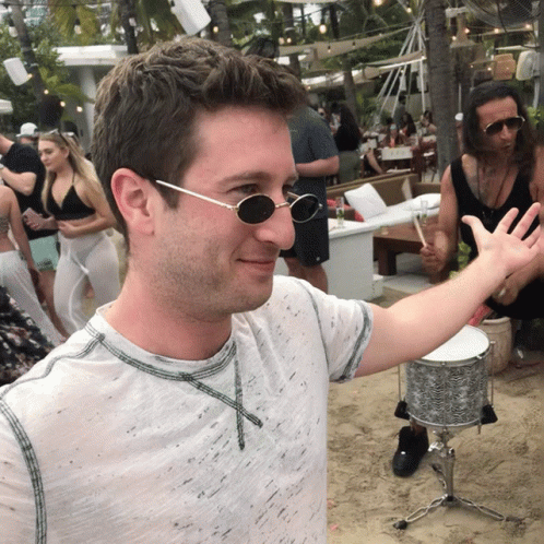 A Man Wearing Sunglasses Is Standing In Front Of A Drum GIF