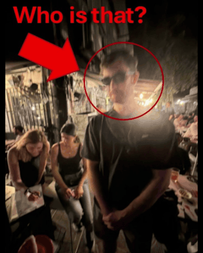 A Man Wearing Sunglasses Is Standing In Front Of A Group Of People With A Red Arrow Pointing To The Man 'S Face GIF