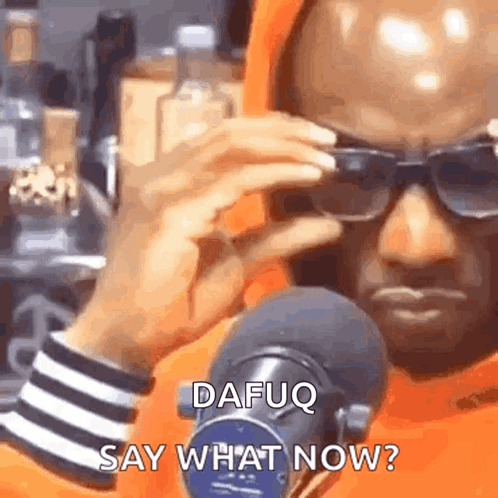 A Man Wearing Sunglasses Is Standing In Front Of A Microphone And Talking Into It . GIF