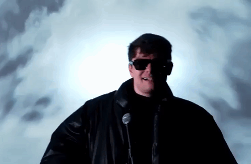 A Man Wearing Sunglasses Is Standing In Front Of A Microphone . GIF
