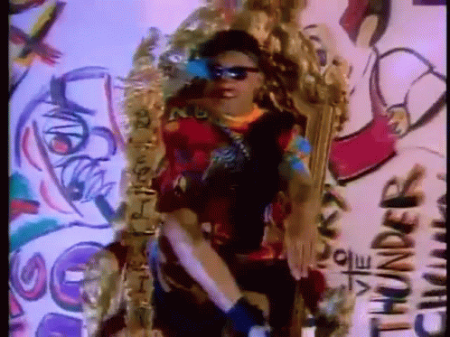 A Man Wearing Sunglasses Is Standing In Front Of A Wall With Graffiti That Says Thunder GIF