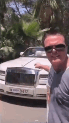 A Man Wearing Sunglasses Is Standing In Front Of A White Rolls Royce . GIF